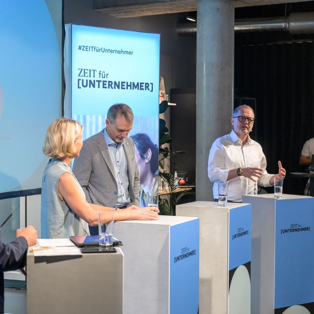 Three people on a podium discussing whilst one of them is speaking